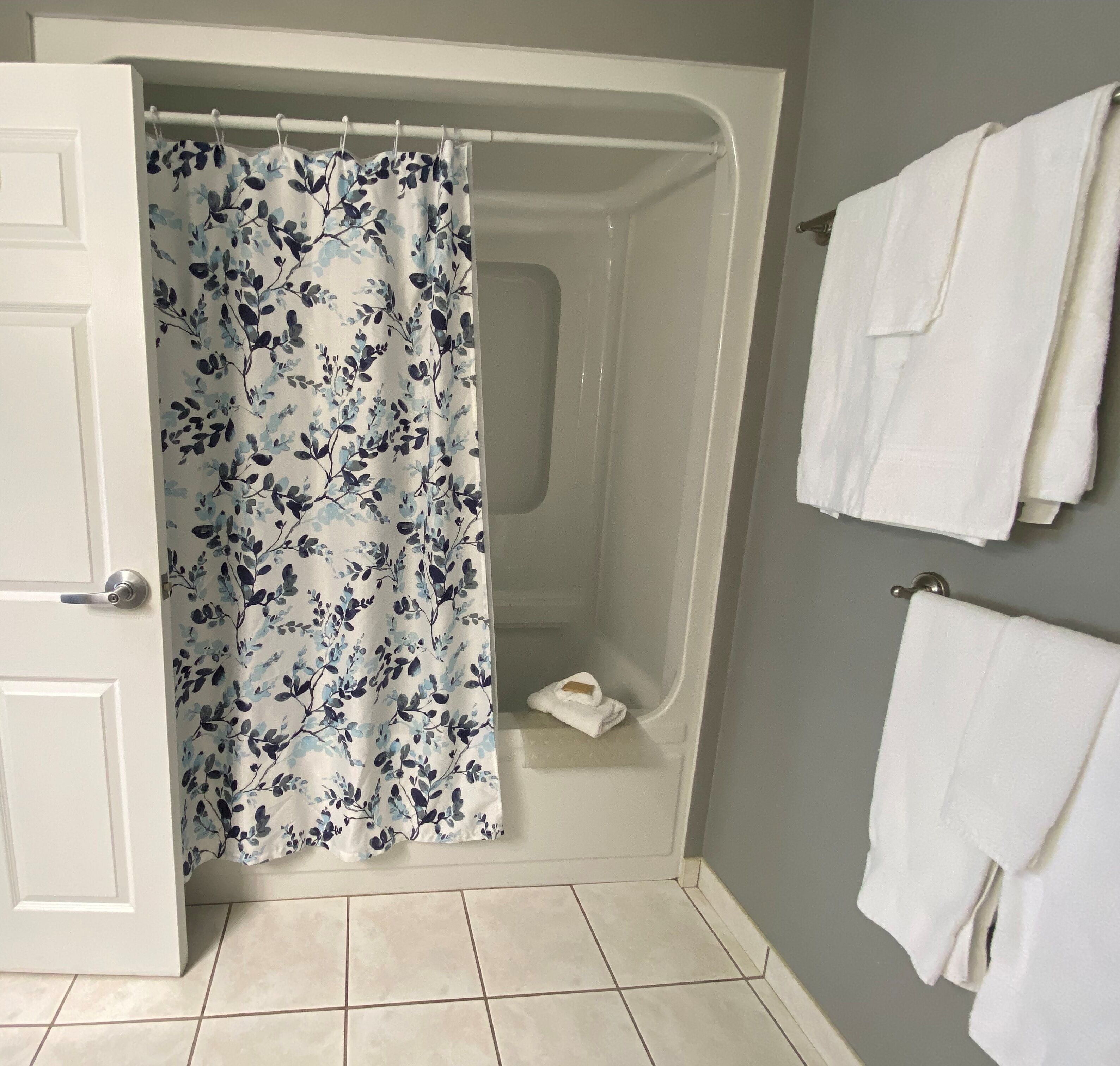 A bathroom with a shower curtain, a bathtub, and two white towels hanging on the wall.
