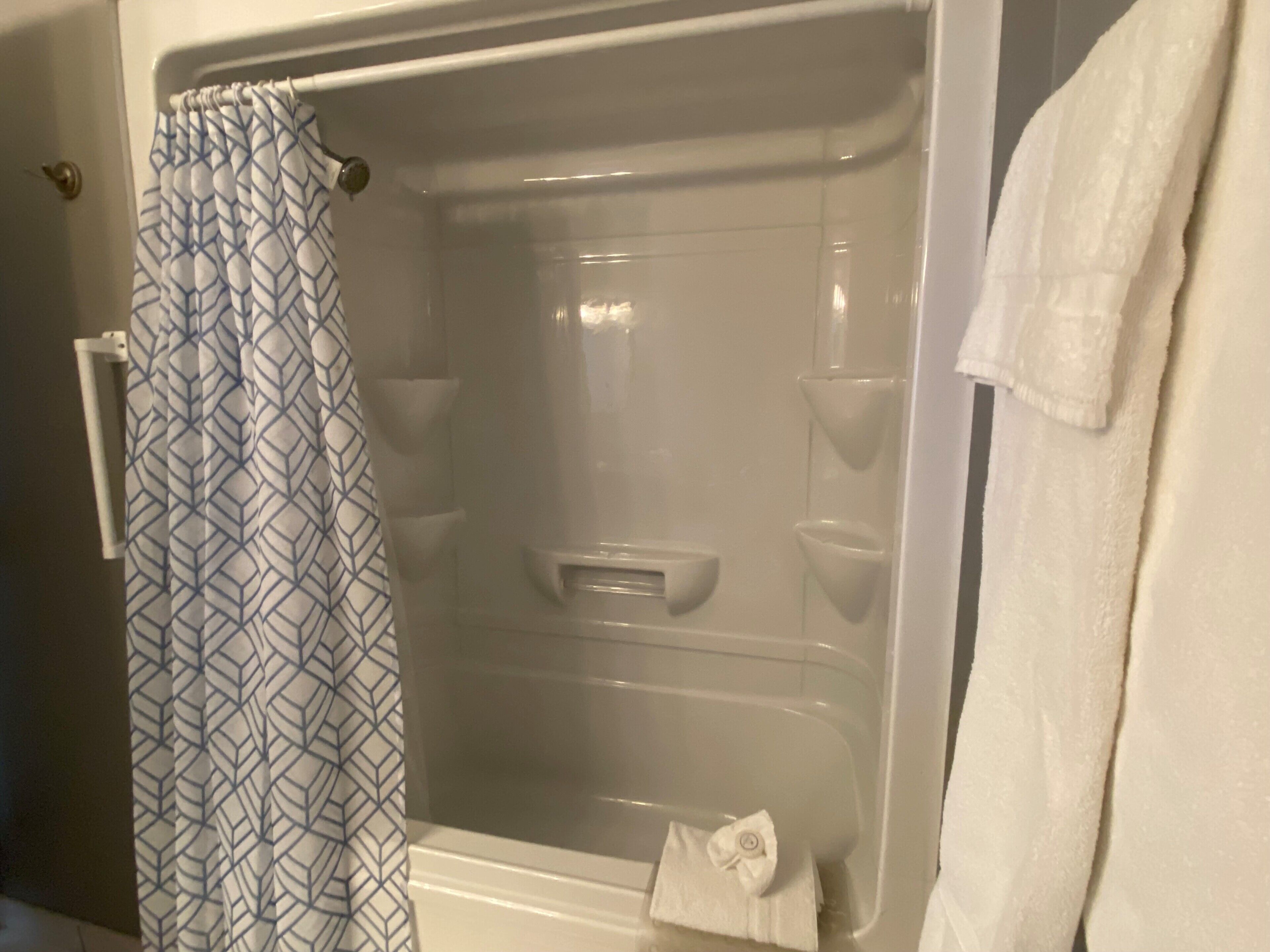 A shower with a patterned curtain, a white towel, and a visible shower control panel.