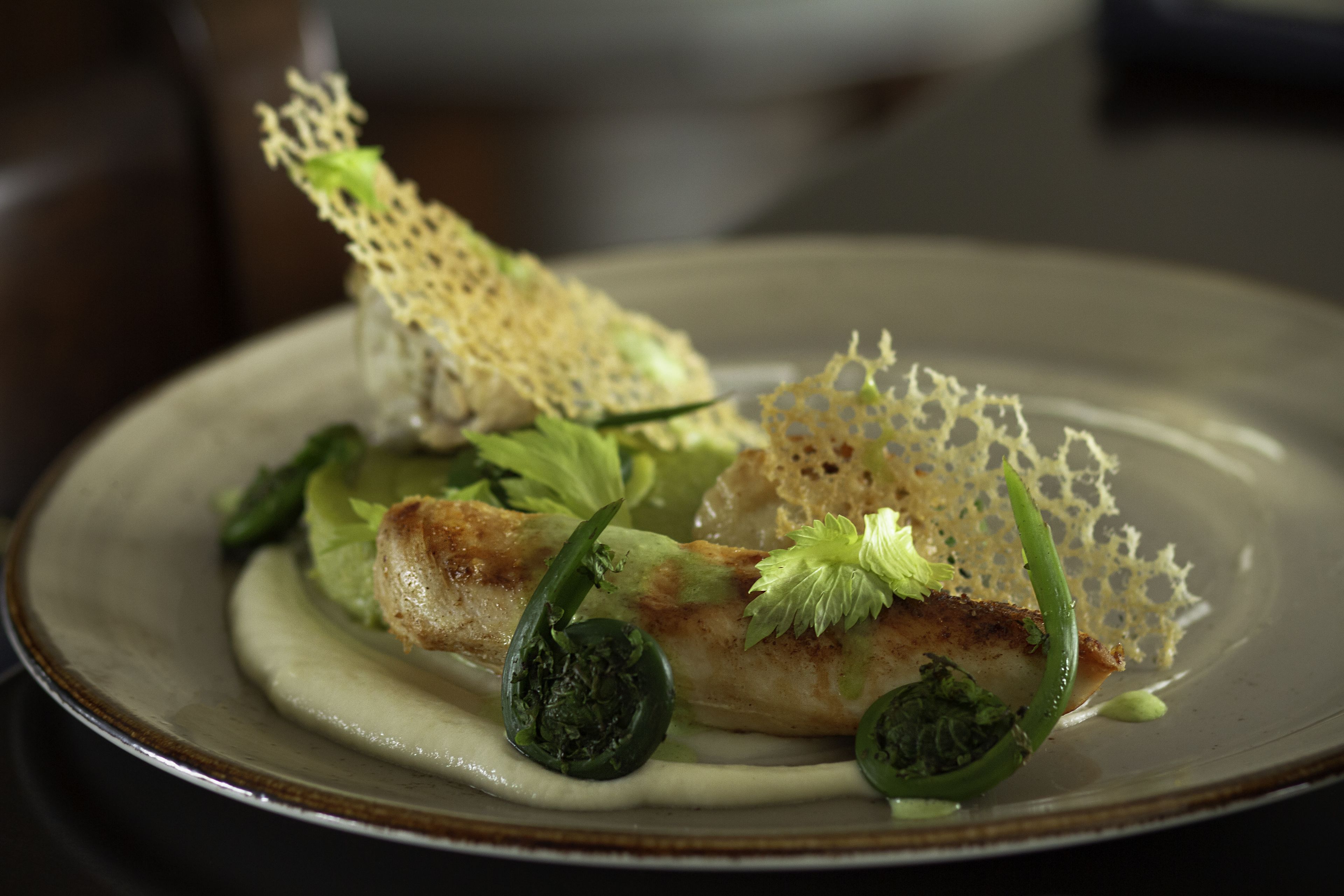 Une assiette de nourriture comprenant un morceau de poisson, des légumes verts et un élément décoratif.
