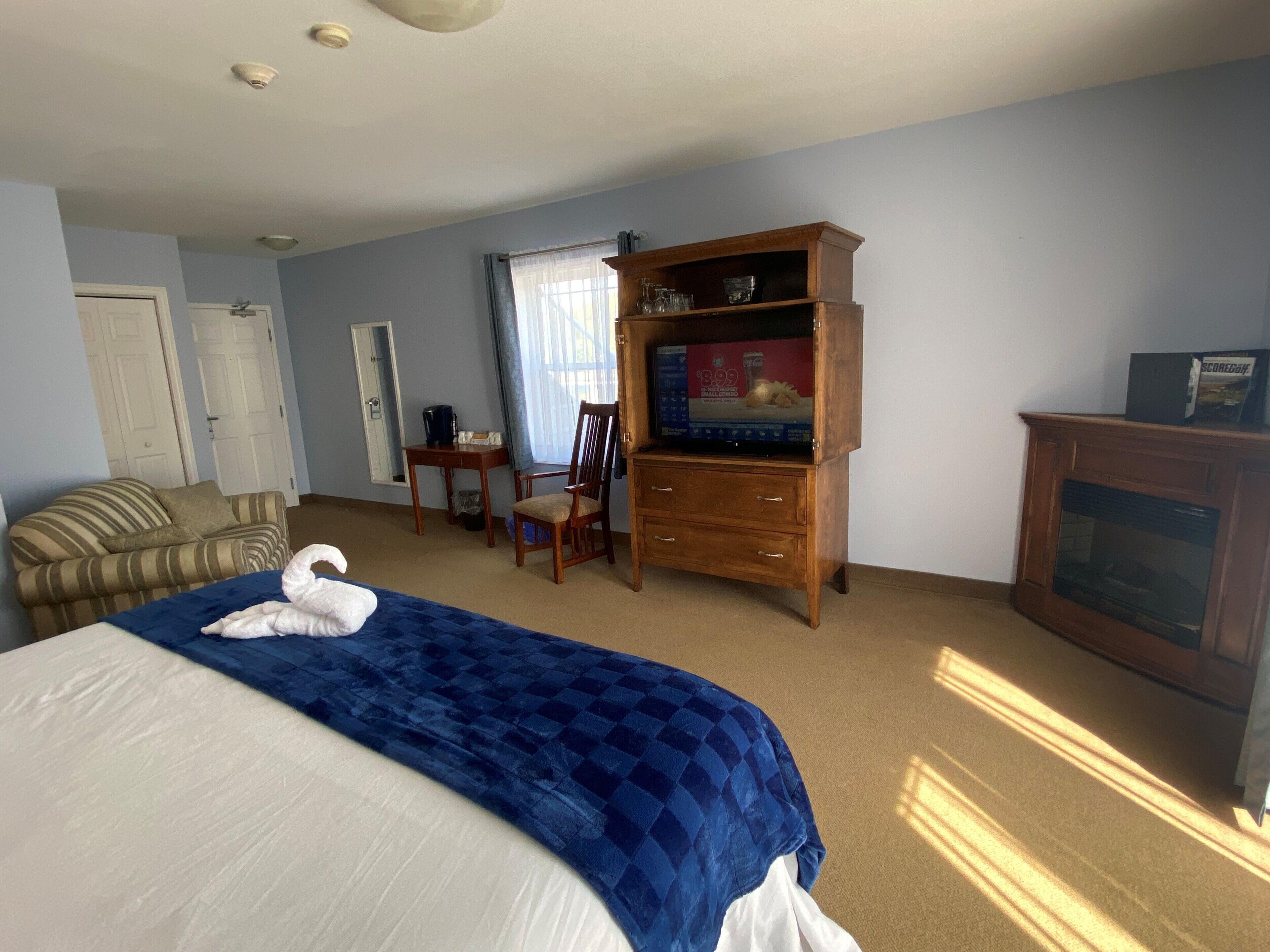 A hotel room with a bed, a wooden TV stand, a chair, a desk, and a fireplace.