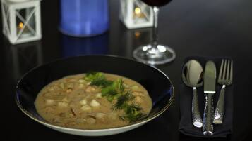 A bowl of soup with a creamy texture and garnished with herbs, accompanied by a glass of red wine, a blue candle, and cutlery on a black table.