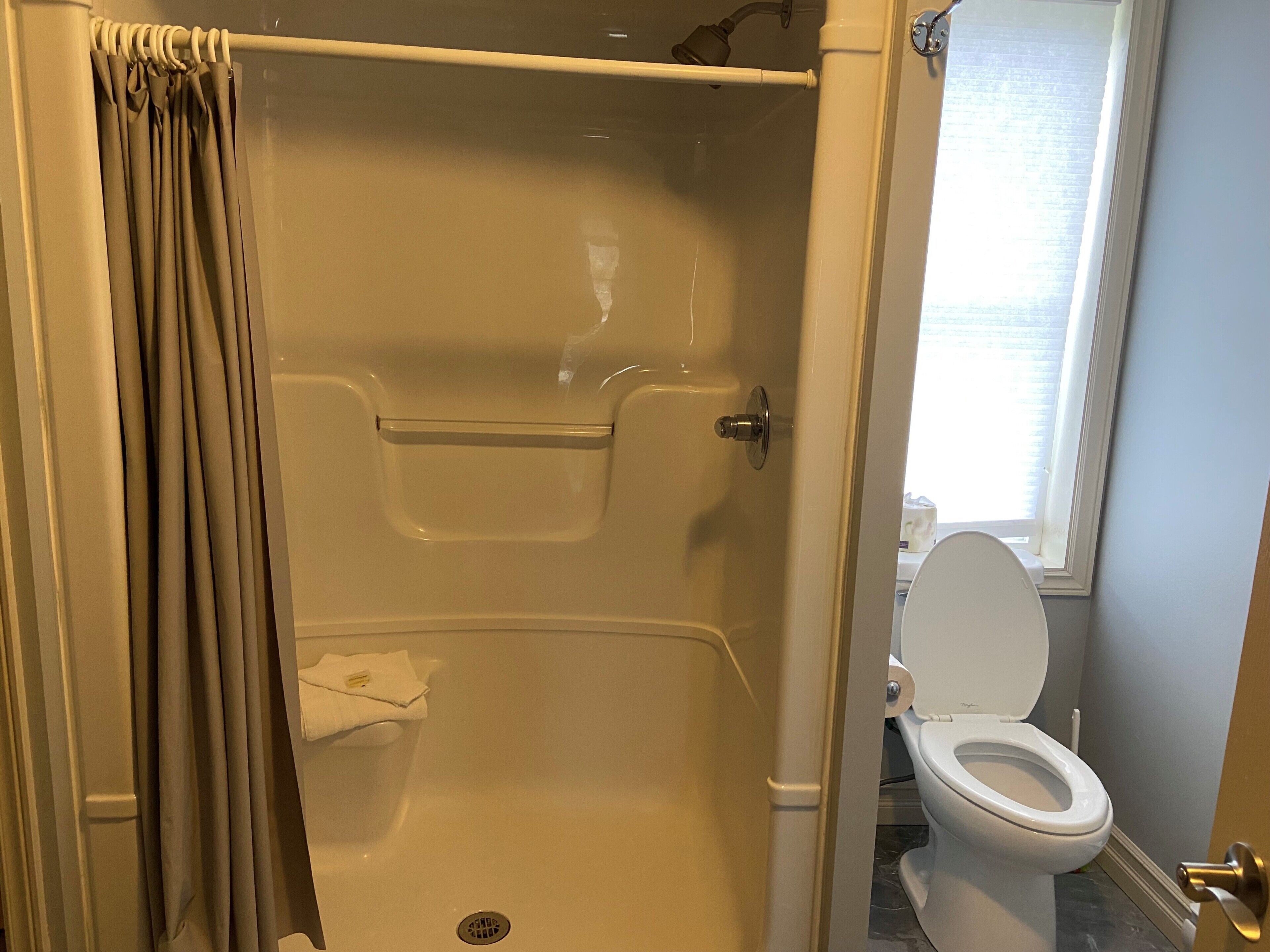 A bathroom with a shower, toilet, and a window.