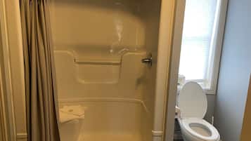 A bathroom with a shower, toilet, and a window.