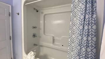 Une salle de bain avec une baignoire, un rideau de douche et une serviette sur le sol.