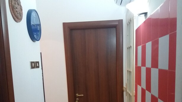 A hallway with a wooden door, a wall clock, and a red and white checkered wall. - B&B Appartamenti Napoli (Naples)