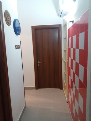 A hallway with a wooden door, a wall clock, and a red and white checkered wall. - B&B Appartamenti Napoli (Naples)