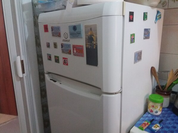 A white refrigerator with various magnets and stickers, a wooden spoon in a jar, and a blue checkered tablecloth. - B&B Appartamenti Napoli (Naples)