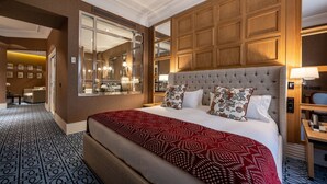 Quarto de hotel com uma cama grande, cabeceira de madeira, um espelho e vista para o banheiro.