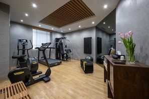 A gym with exercise equipment, a wooden floor, a desk with a vase, and a wall-mounted TV.