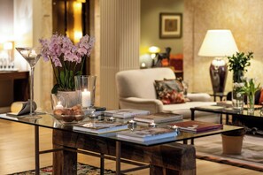 A well-lit, elegantly furnished living room with a glass coffee table, books, candles, and decorative flowers.