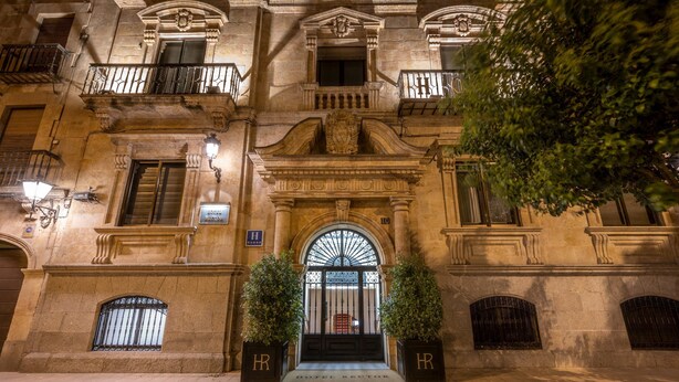 Um edifício histórico com uma entrada imponente, varandas ornamentadas e uma placa indicando que é um hotel.