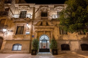 A historic building with a grand entrance, ornate balconies, and a sign indicating it is a hotel.