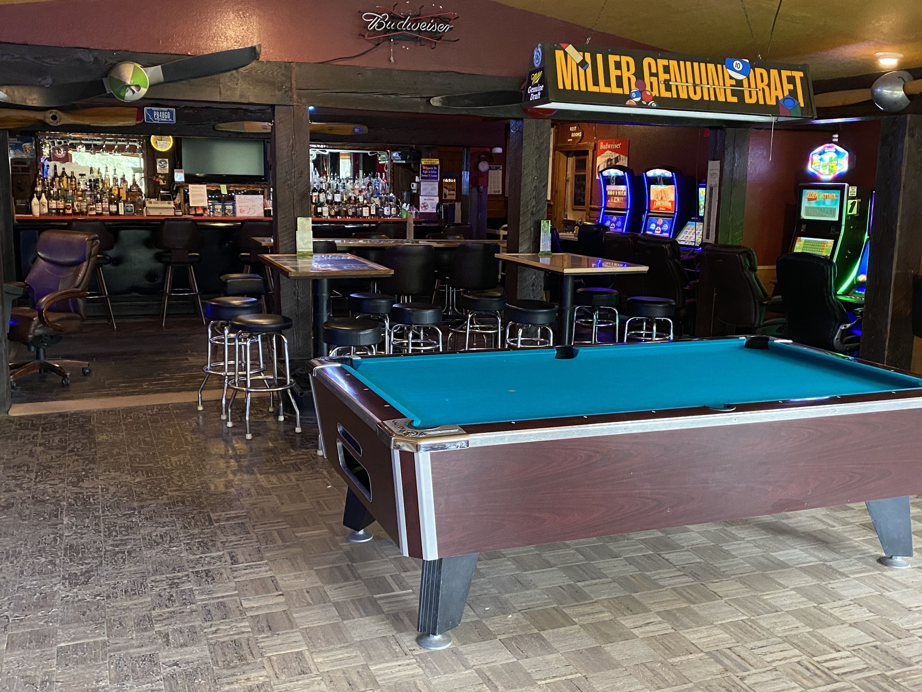 A bar area with a pool table, bar stools, and arcade games.