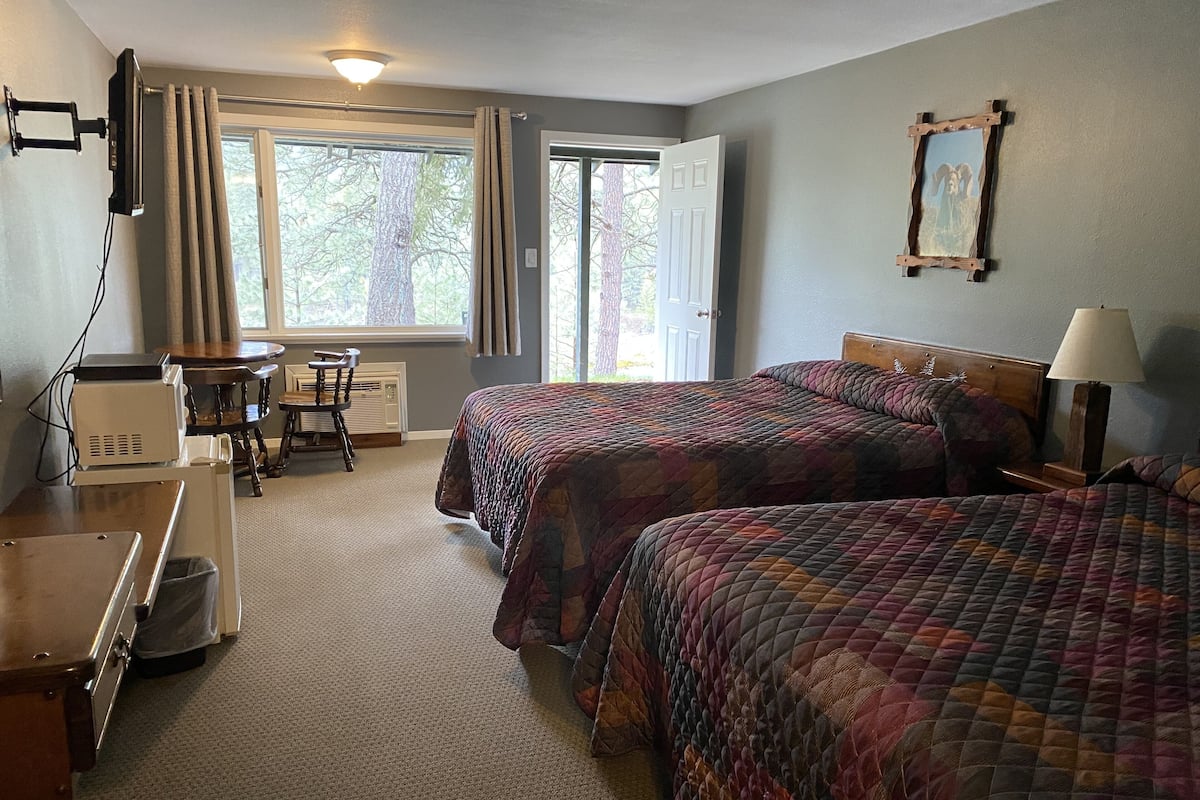 A hotel room with two beds, a desk, a chair, a TV, and a window with curtains.