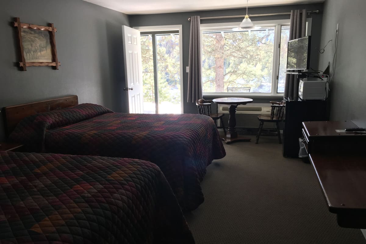 A hotel room with two beds, a desk, a chair, a TV, and a window with curtains.