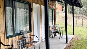 A wooden building with a covered porch, two doors, and two chairs.