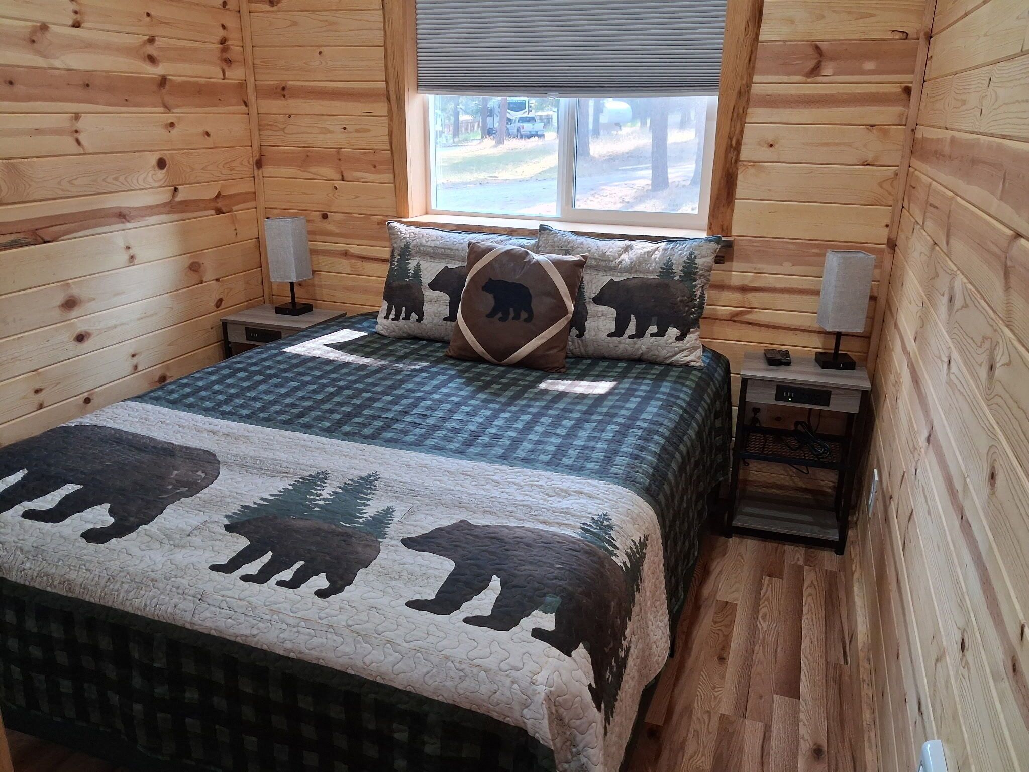 Una camera da letto in una baita di legno, con un letto, due comodini, una finestra e vista all'esterno.
