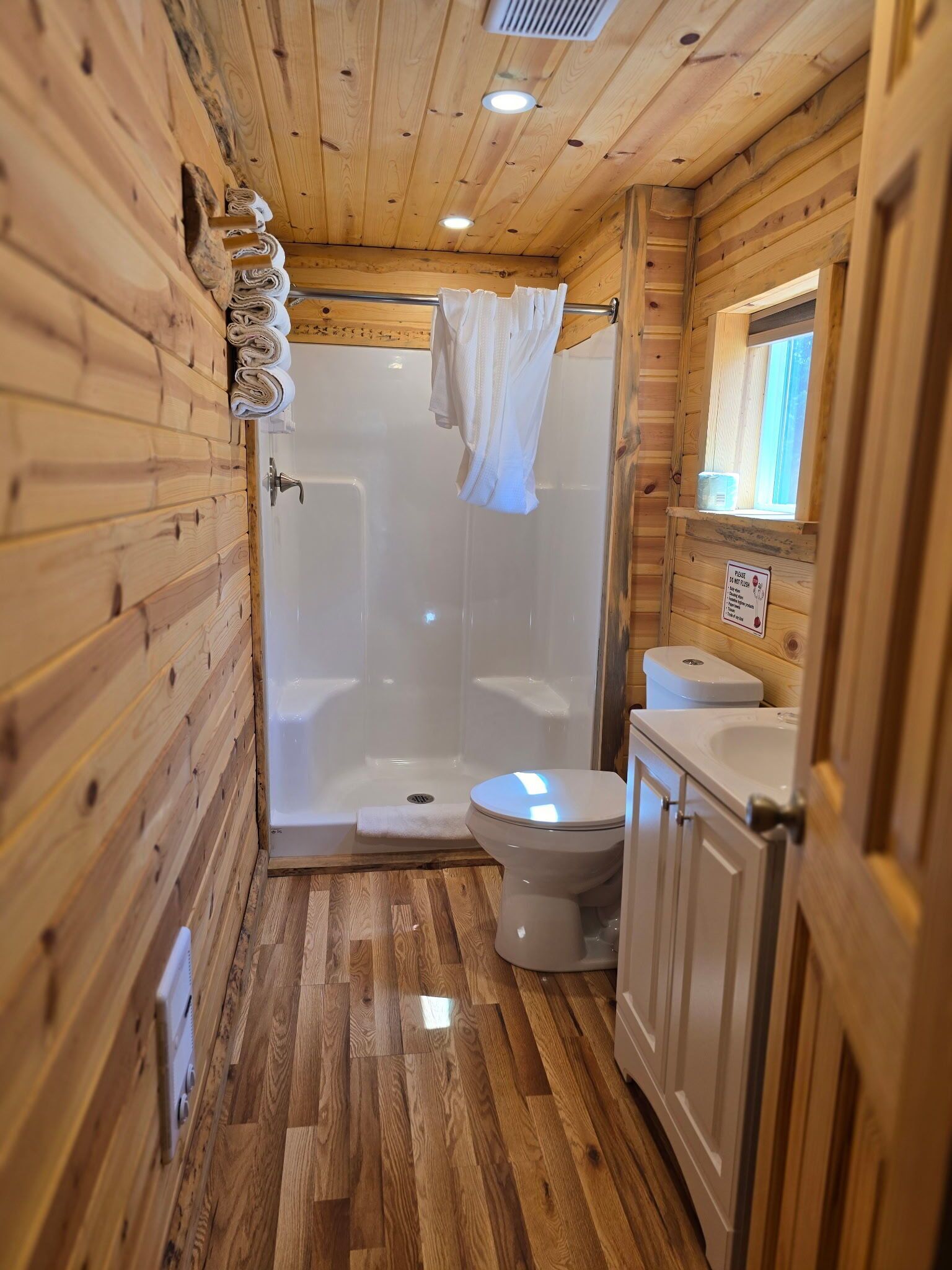 Une salle de bain rustique, située dans une cabane en bois, équipée d’une douche, de toilettes et d’un lavabo.