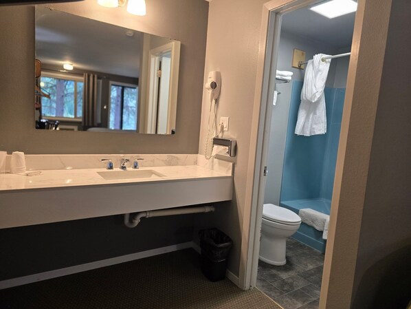 A bathroom with a sink, mirror, hairdryer, and toilet.