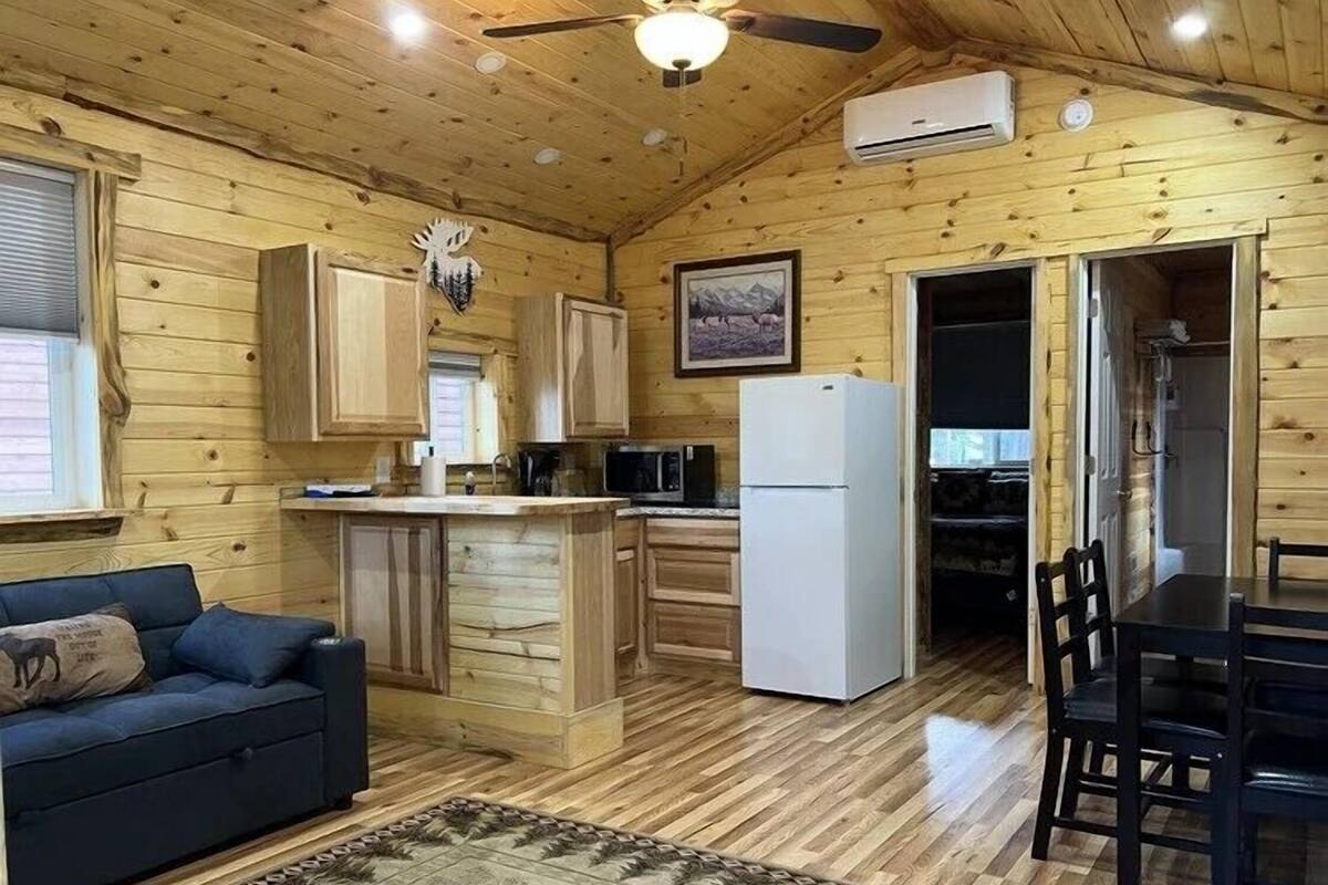 A wooden cabin interior with a kitchen, dining area, and a sofa.