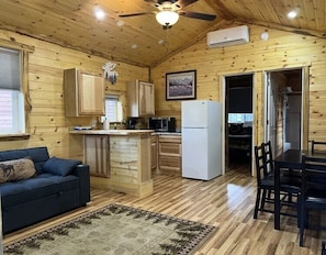 A wooden cabin interior with a kitchen, dining area, and a sofa. - Rimrock Lodge (Thompson Falls)