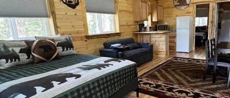 Una habitación tipo cabaña de troncos con cama, sofá y zona de cocina.