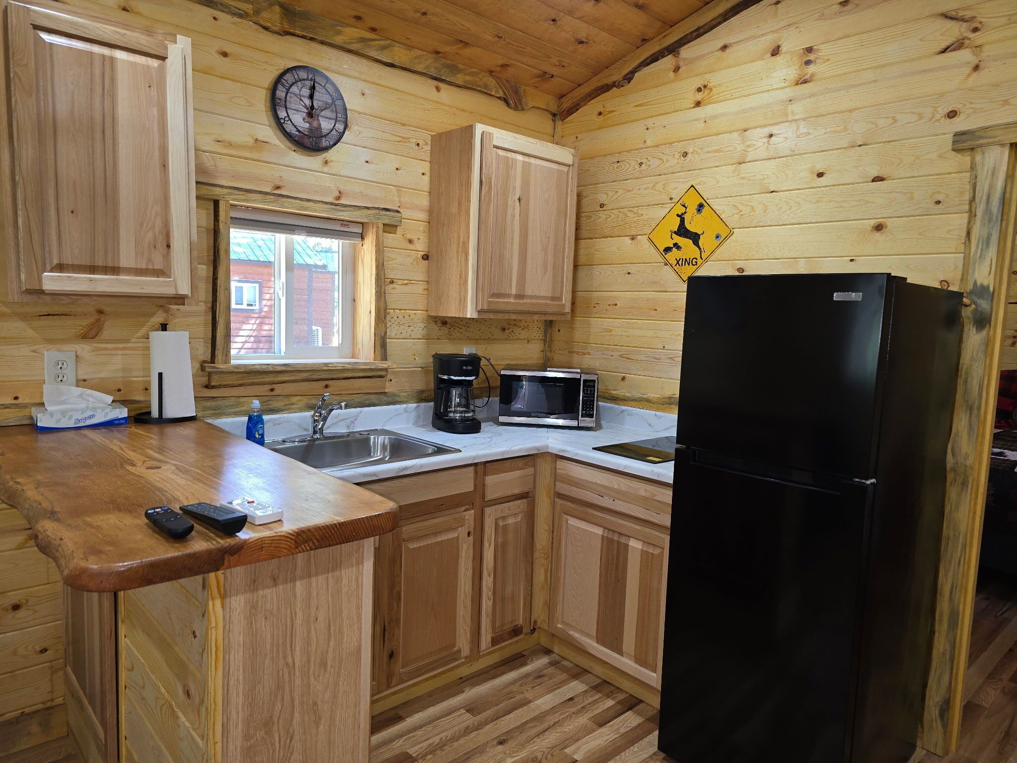 Cocina de cabaña de madera con un lavamanos, un refrigerador negro, una cafetera y un reloj en la pared.