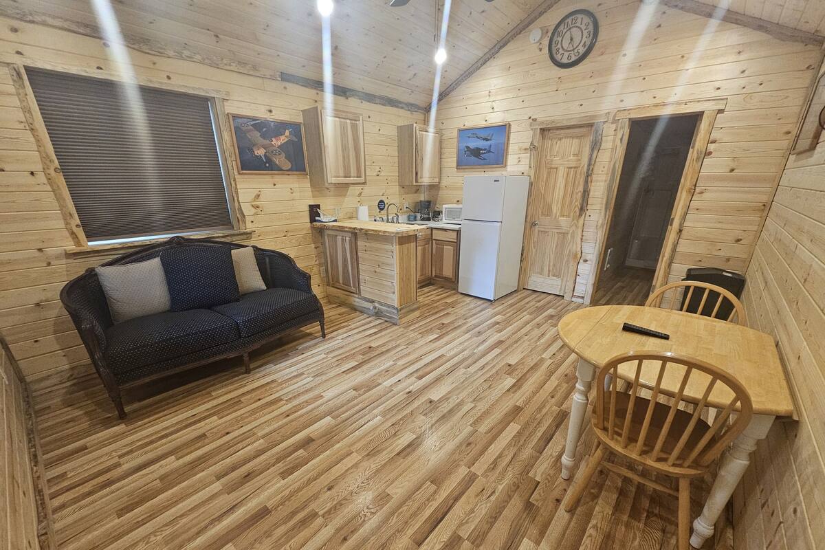 A cozy cabin interior with a wooden floor, a sofa, a dining table, and a kitchen area.