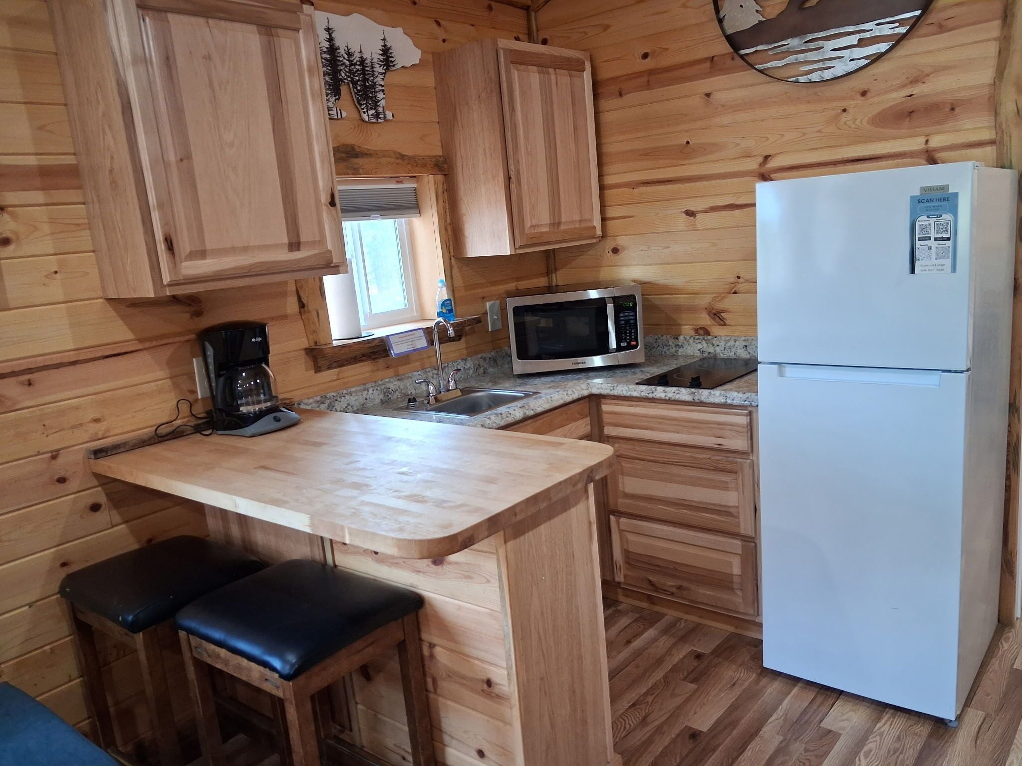 A compact kitchen with wooden cabinets, a microwave, a refrigerator, and a coffee maker.