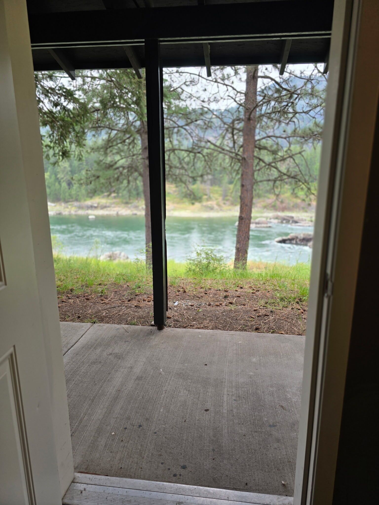 Una puerta que da a un espacio al aire libre techado, con vistas a un río y árboles.