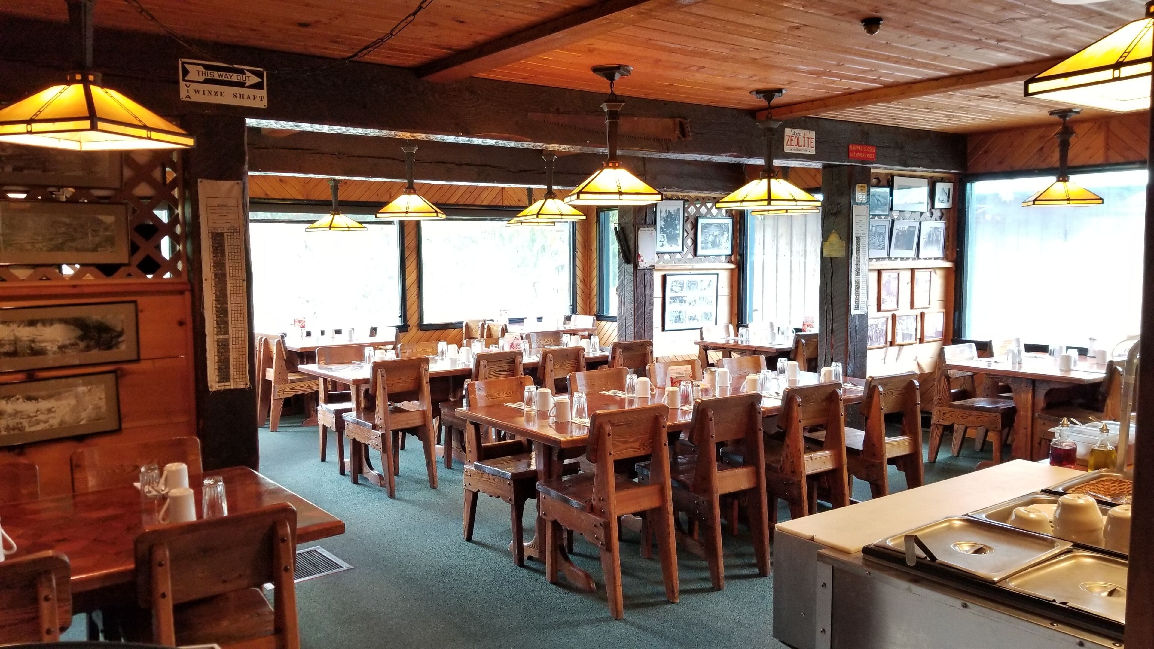 A restaurant with wooden tables and chairs, hanging lamps, and framed pictures on the walls.