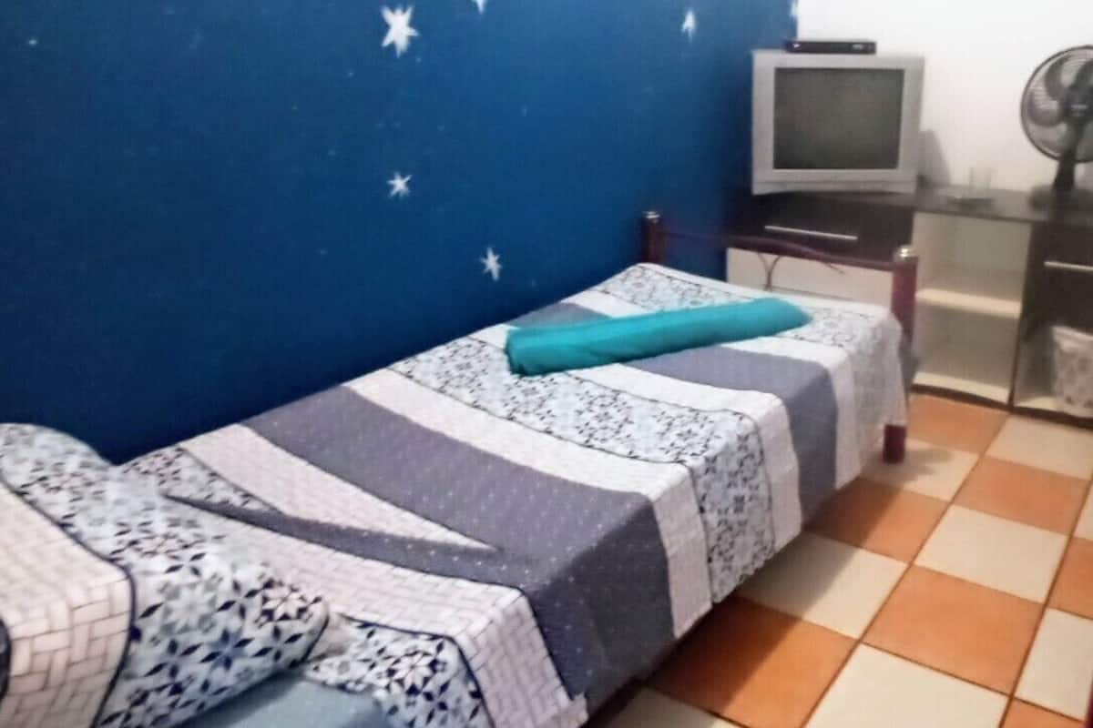 A small room with two single beds, a TV, a fan, and a tiled floor.