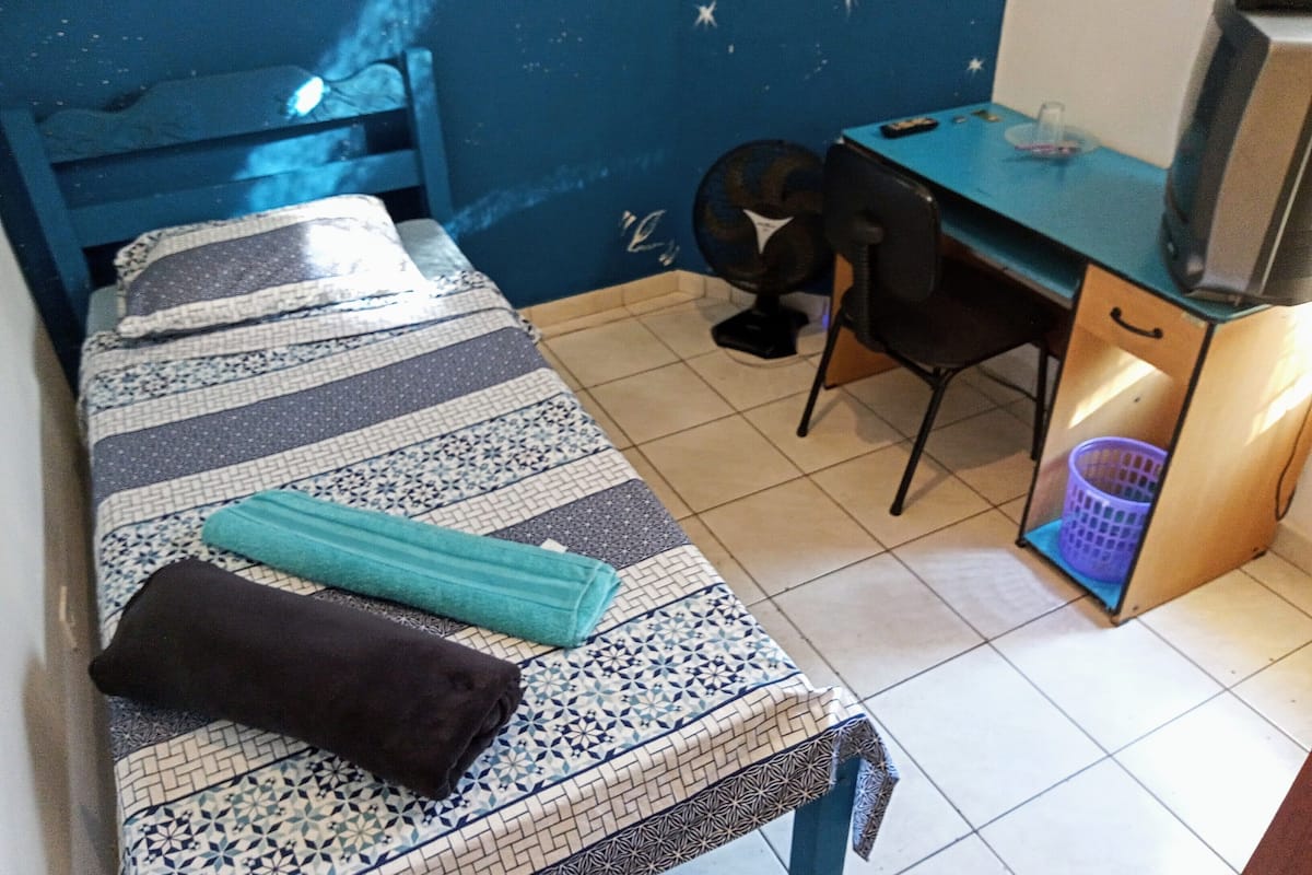 A bedroom with a bed, a desk, a chair, and a TV.