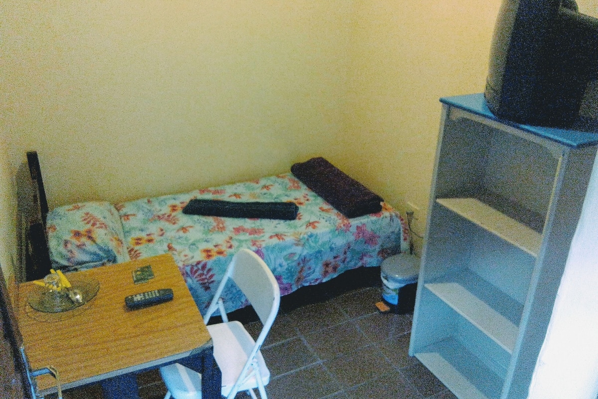 A small room with a bed, a desk, a chair, and a TV on a stand.