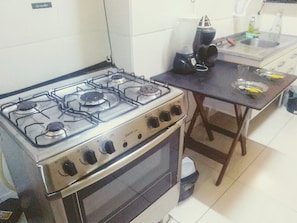 Una cocina con estufa a gas, horno y una pequeña mesa con licuadora.