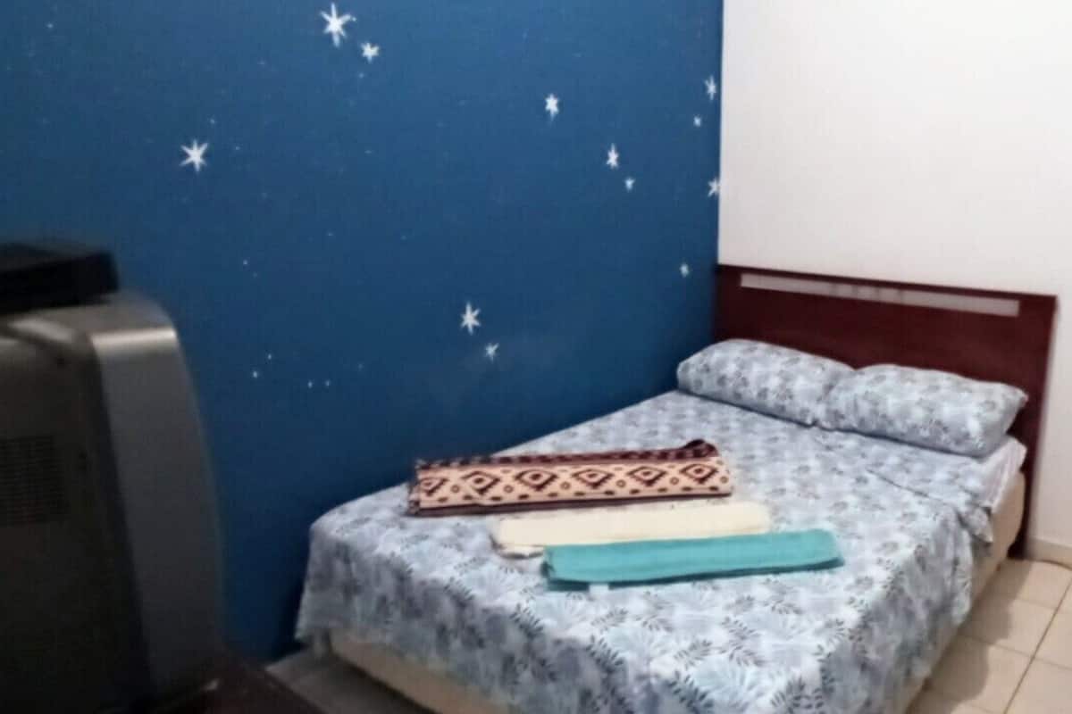 A small, single-bed room with a blue wall and star-patterned wallpaper. A heater is on the left, and a fan is on the right.