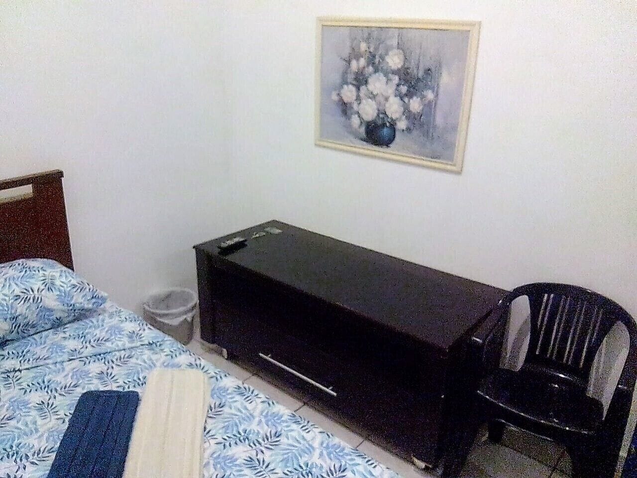 Um quarto com uma cama, um móvel de armazenamento preto, uma cadeira e um quadro na parede.