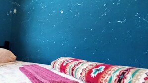Ein Schlafzimmer mit einem Bett, einer gemusterten Decke und einer blauen Wand mit sternartigen Mustern.