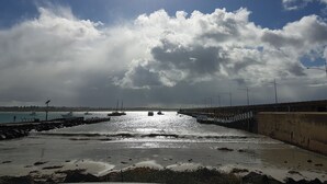 A beach with a concrete walkway, calm water, and boats in the distance. - Gillies st Apartments (Warrnambool)