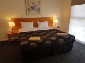 A hotel room with a large bed, two bedside lamps, a nightstand, a framed picture on the wall, and a window with curtains. - Gillies st Apartments (Warrnambool)