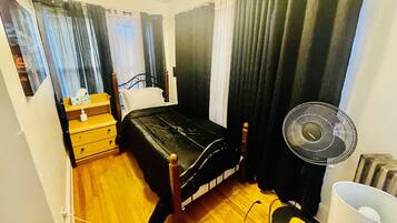 Una camera da letto con un letto, un comodino con una lampada, una ventola e una finestra con tende.