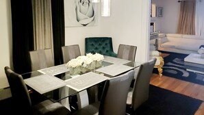 A dining area with a glass table, grey chairs, and a vase of white flowers. There is a green upholstered chair, a chandelier, and a painting of a rose on the wall. - Cozy & Spacious Entire Home in Springfield (Springfield)