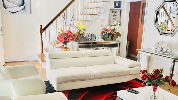 A modern living room with a white sofa, a coffee table, and a red and black rug. There is a staircase with a white railing leading to a second floor. - Cozy & Spacious Entire Home in Springfield (Springfield)