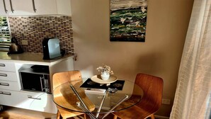 Una cocina compacta con microondas, hervidor y una pequeña mesa con sillas. Hay un jarrón decorativo sobre la mesa.