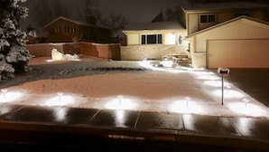 A residential driveway with snow, a garage, and a house with a lit exterior. - Cozy House With Hot Tub and Gaming Room (Colorado Springs)