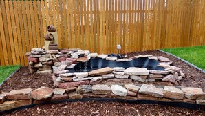 A garden with a stone fire pit and a small waterfall. - Cozy House With Hot Tub and Gaming Room (Colorado Springs)