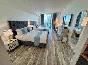 Habitación de hotel con dos camas, un escritorio, un aparador, un espejo y un televisor.