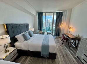 A hotel room with a large bed, a desk, a chair, and a view of the cityscape.