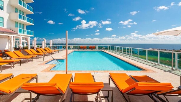 A poolside area with orange lounge chairs and a clear view of the ocean. - Balcony Ocean Views | Pool, Gym, Wi-Fi & Parking (Miami)
