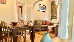 Un comedor con una mesa y sillas de madera, un jarrón y un sofá al fondo.